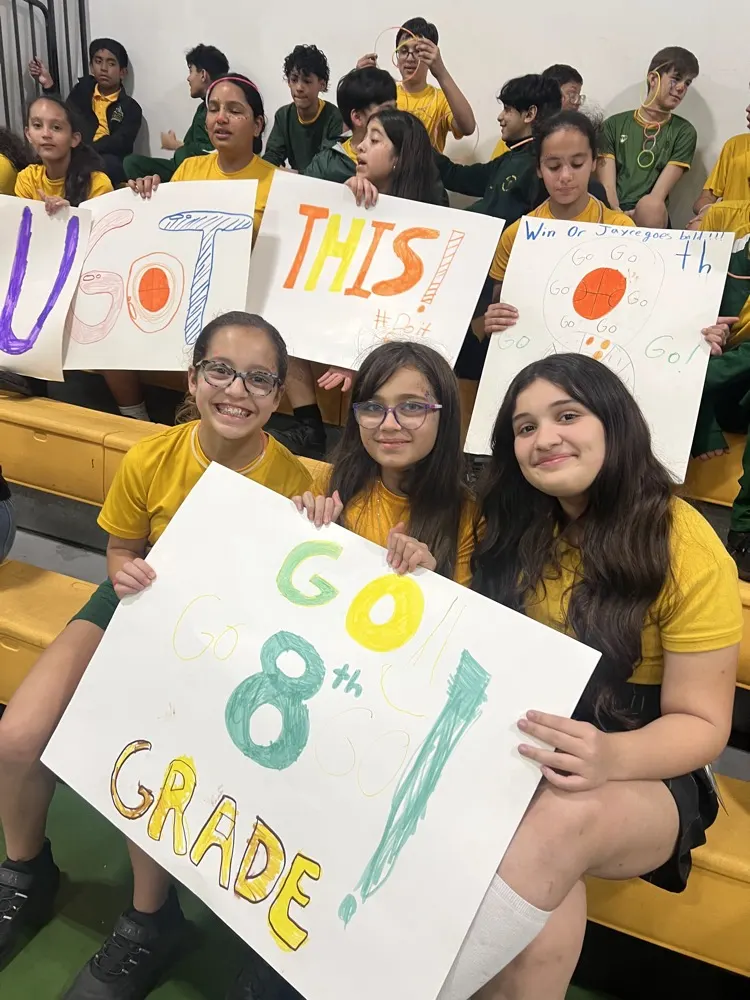 Holy Redeemer sixth graders in the bleachers holding hand-painted signs cheering on the eighth grade