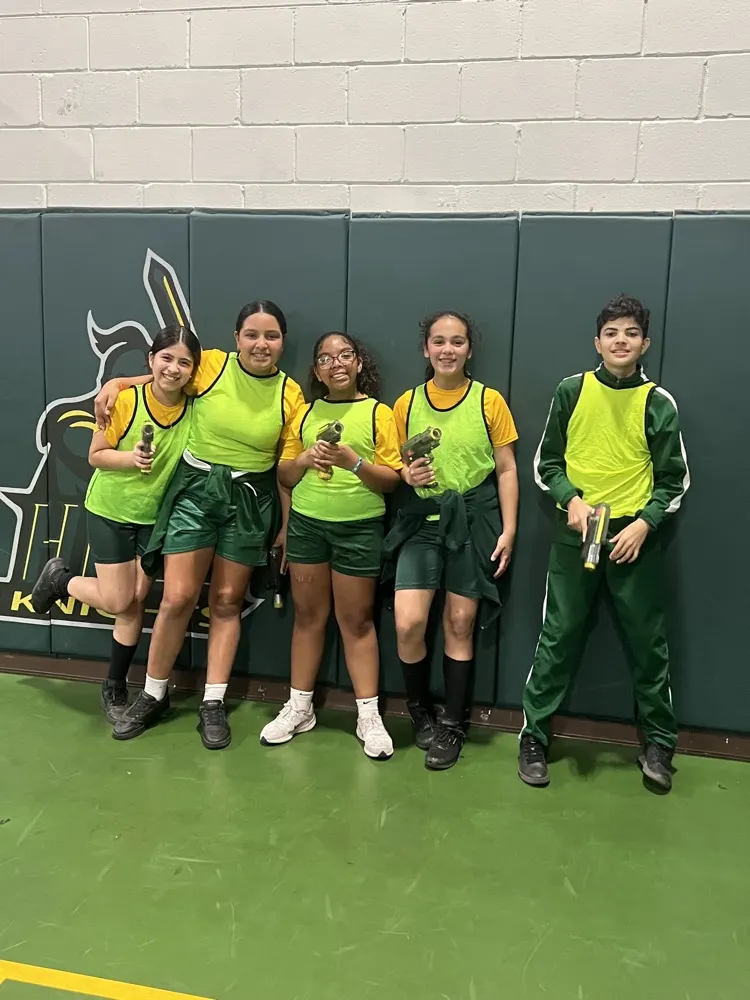 Five Holy Redeemer students in green laser tag vests holding laser tag blasters in the school gym